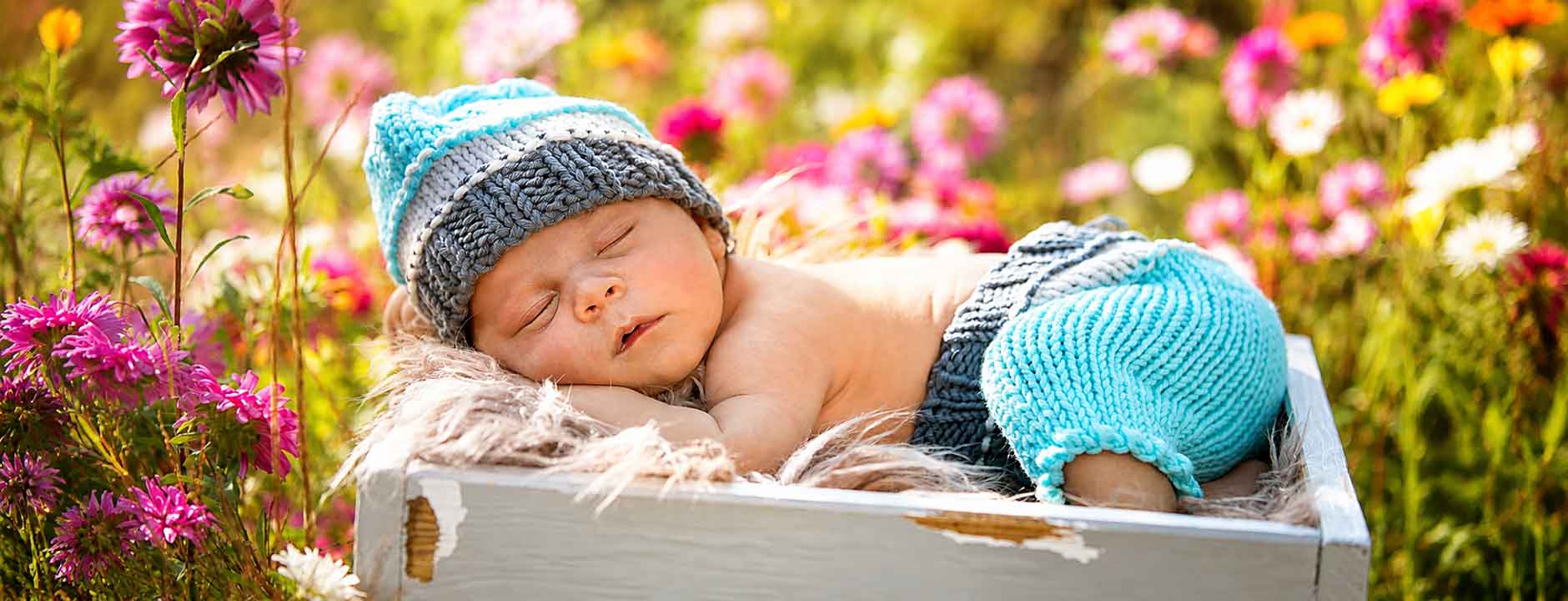  Schlafendes Baby in blau gestrickter Mütze und Hose in Geschenkbox mit Blumen zur Geburt