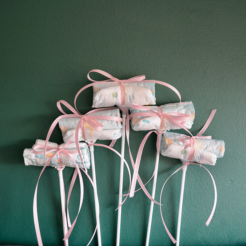 Fünf Windel Einstecker mit rosa Schleifen auf Stäben, dekoratives Accessoire für Baby It's a Girl Blumenversand zur Geburt.