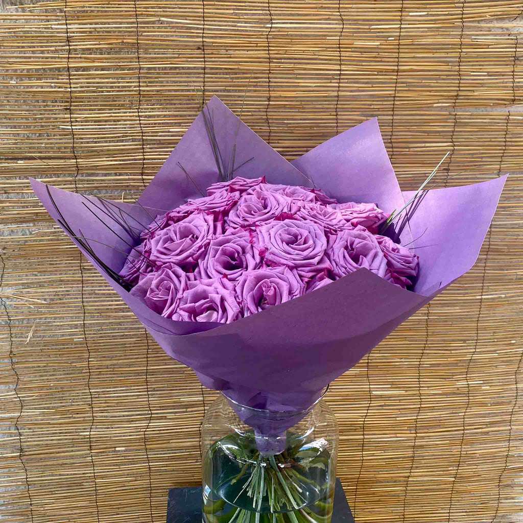 Üppiger Strauß aus lila Rosen mit grünen Ziergräsern und violetter Verpackung