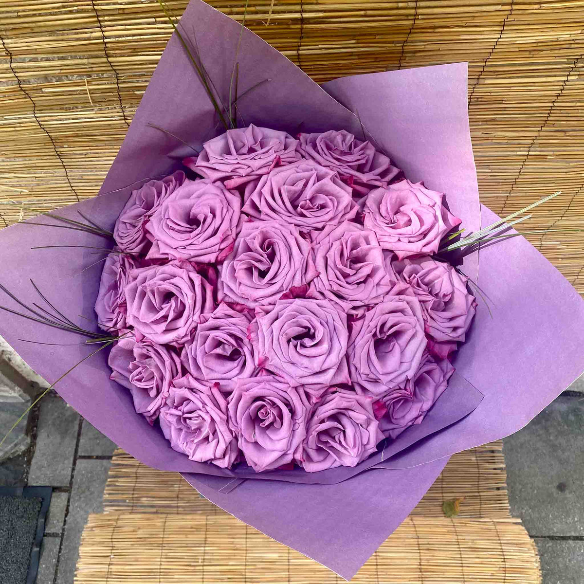 Purple rose bouquet with delicate green ornamental grasses and matching purple wrapping